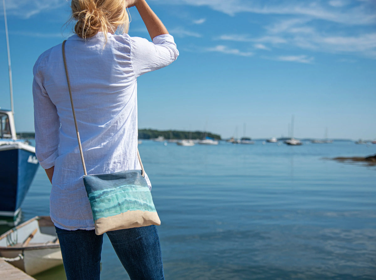 small crossbody bag with shoreline tie dye design worn by woman on new england coast harbor