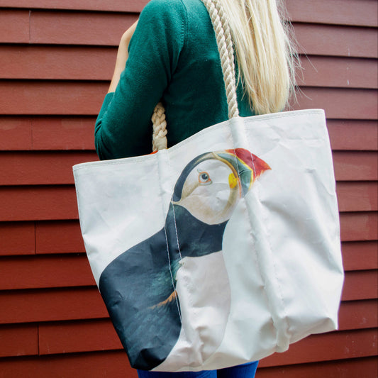 A person carrying a white Puffin Medium Tote by Sea Bags with rope handles featuring an Atlantic Puffin Audubon illustration.