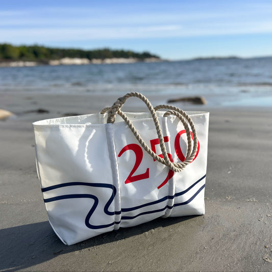 White bag with red text on a sandy beach with ocean in the background