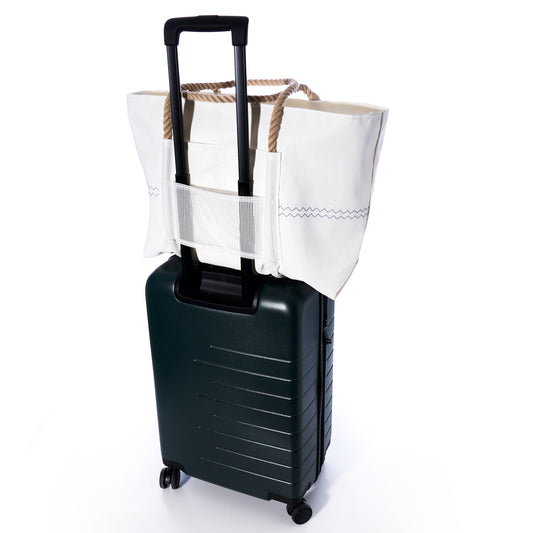 A Custom Monogram Trolley Sleeve Tote by Sea Bags, featuring rope handles in white, is secured to the extended handle of a dark green rolling suitcase against a white background.
