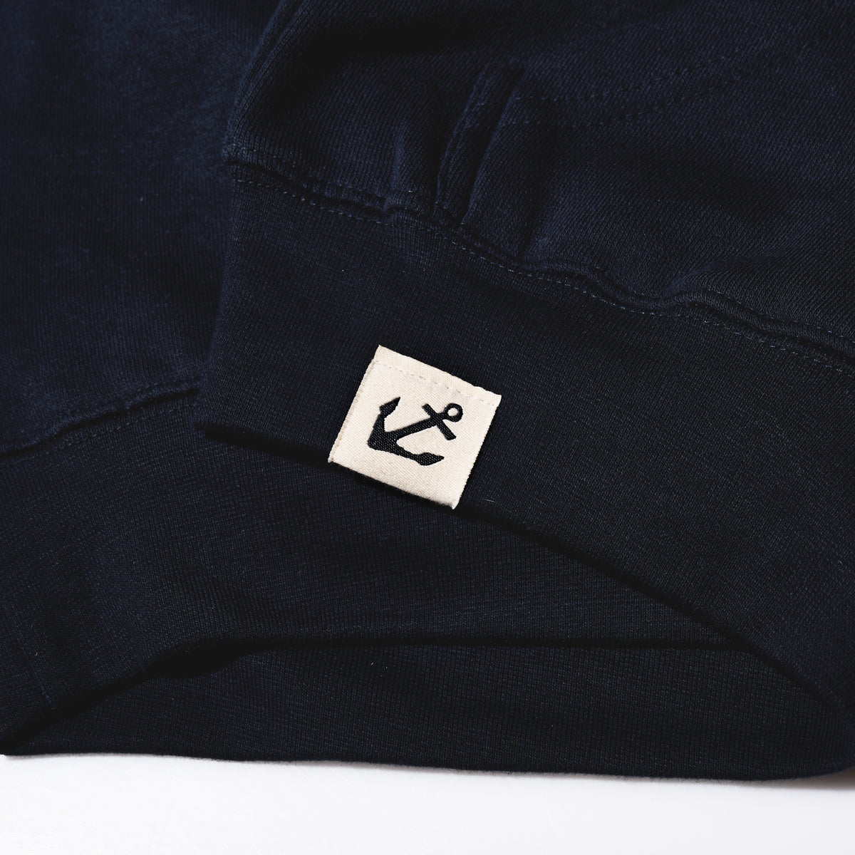 Dark blue Sea Bags Sailing Team Hoodie sleeve with a small cream-colored tag on the cuff featuring a Sea Bags anchor icon.
