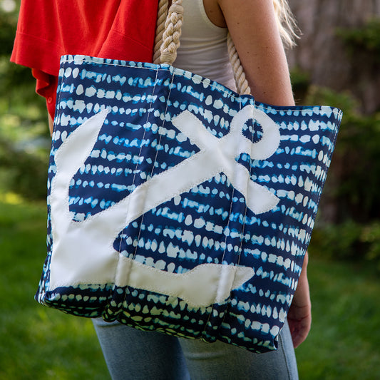 A person carries the Sea Bags White Anchor on Shibori Print Tote, featuring a bold anchor design and sturdy rope handles, made from recycled sail cloth. Grass and trees are visible in the background. by Sea Bags