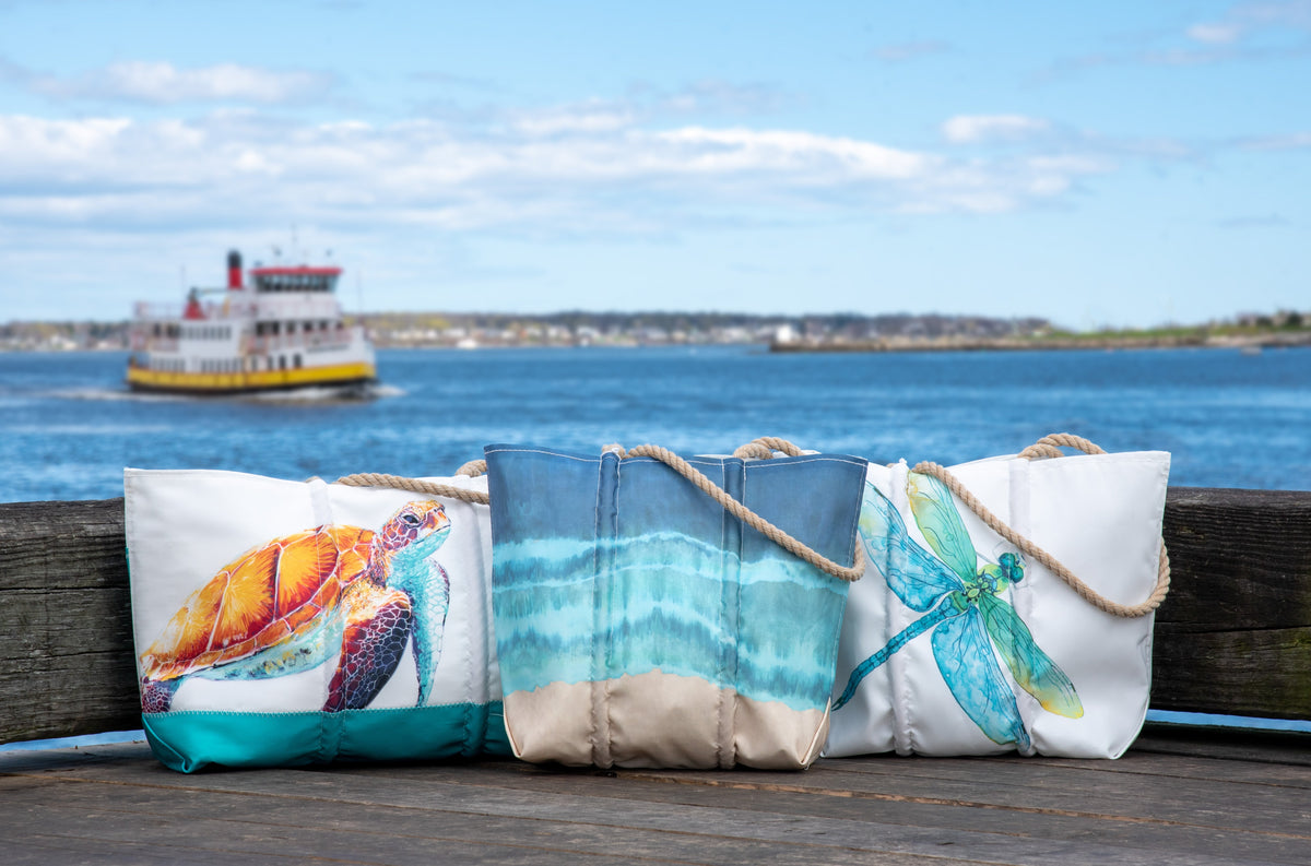 three recycled sail totes on a pier overlooking a waterfront town