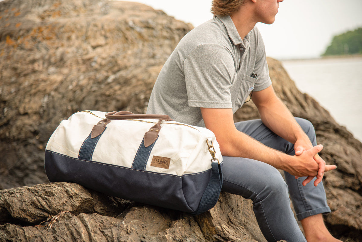 a man on a rocky coast looking at the ocean with a chebeague  travel duffel