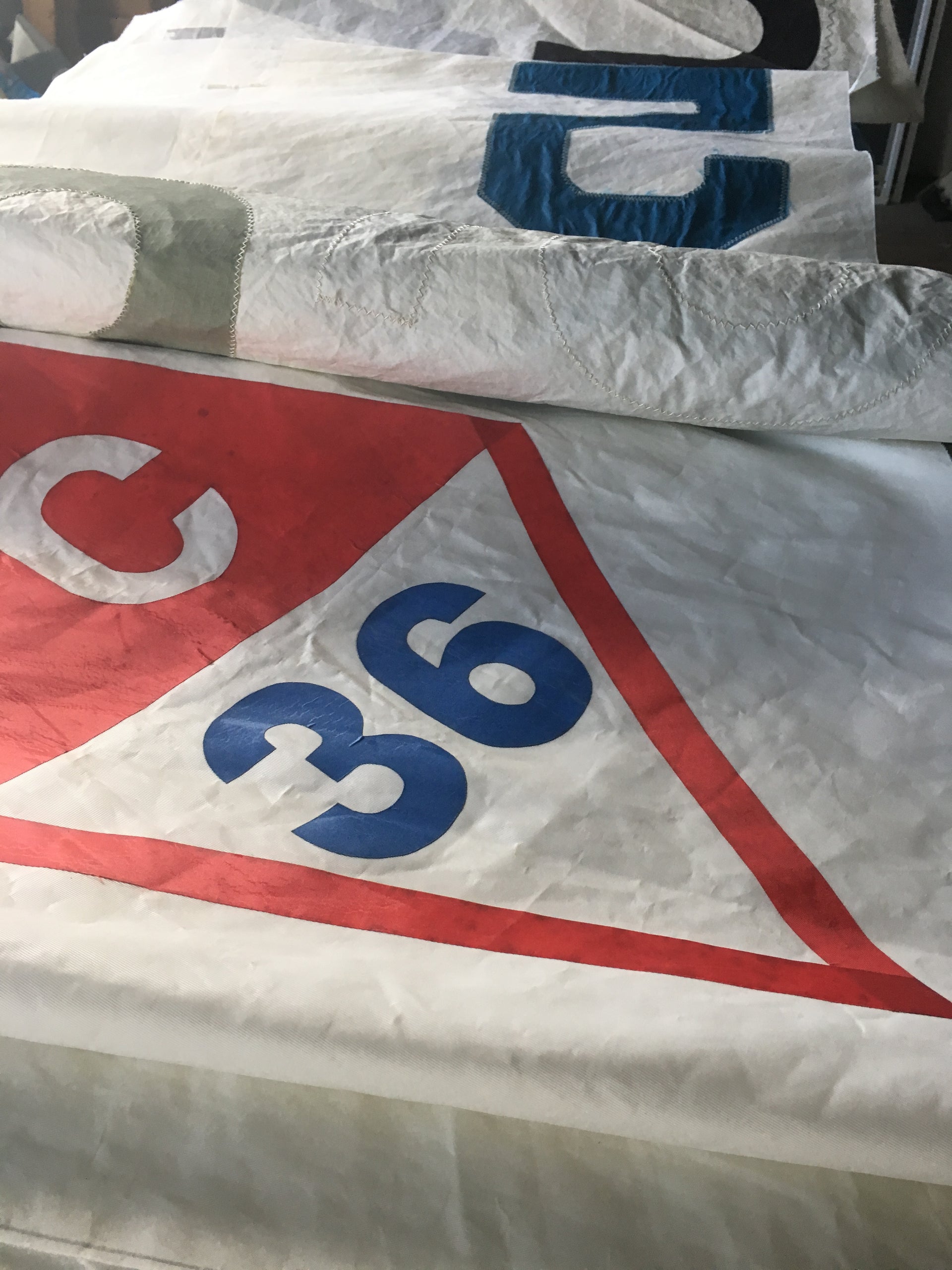 Close-up of stacked sailboat sails, including one featuring a red triangle, the letter C, and the number 36 in blue - ideal material Sea Bags uses for crafting unique sail bags.