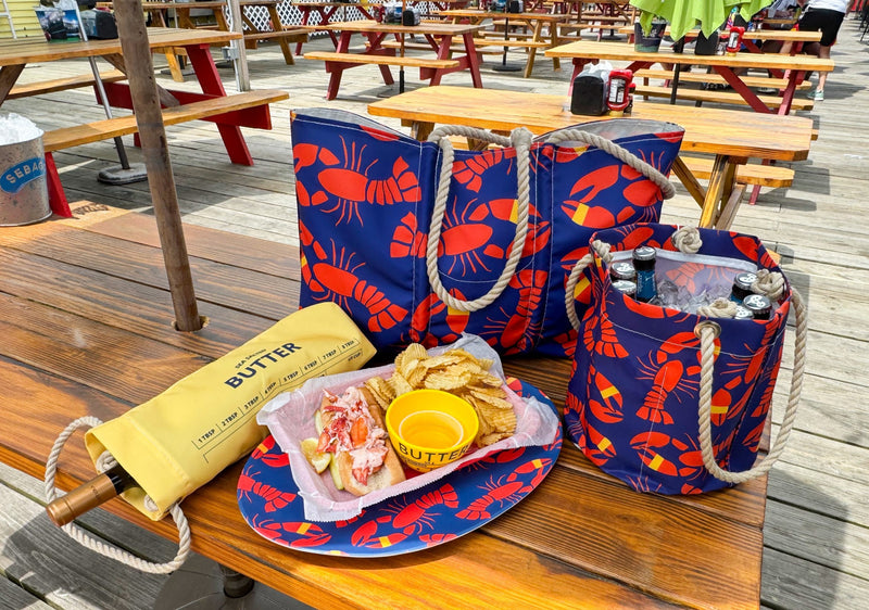 Outdoor setting with lobster-themed bags, food, and drinks on a wooden table.