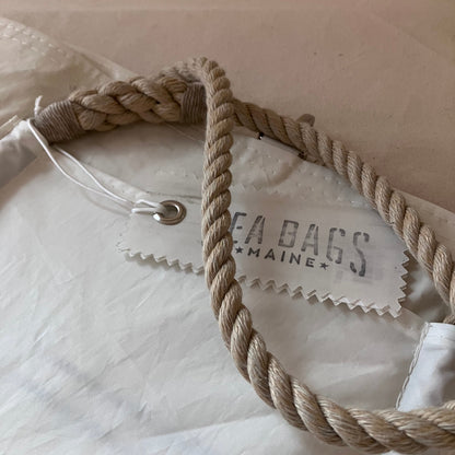 Close-up of a white fabric bag with a thick twisted beige rope handle and a sewn-on brand tag reading SEA BAGS MAINE.