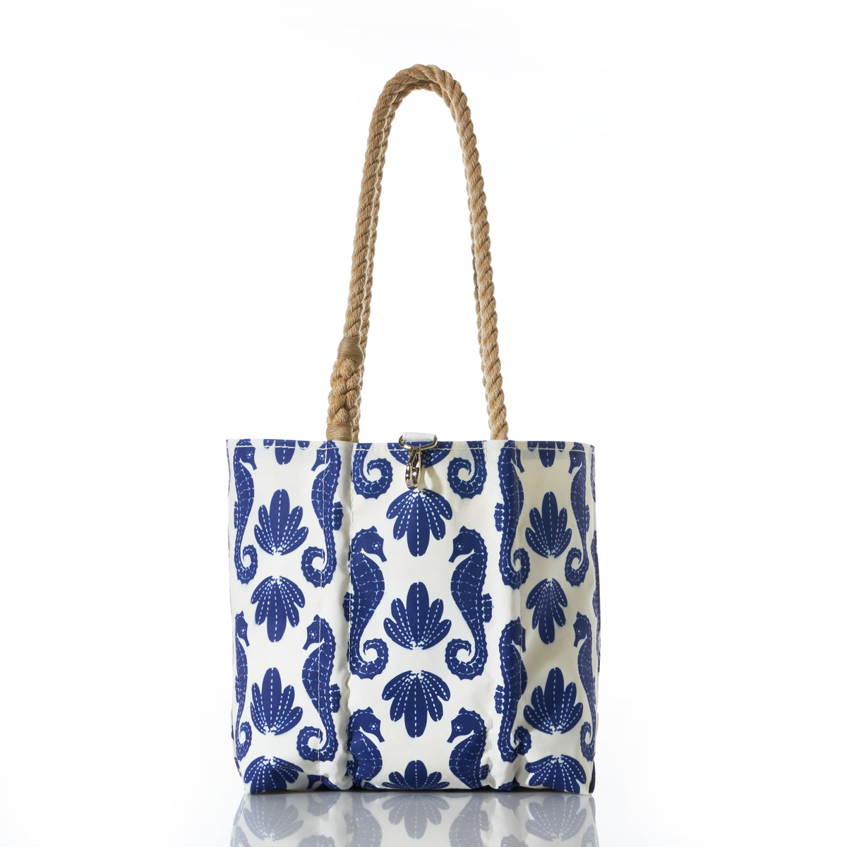 The Blue Sea Horse Print Handbag by Sea Bags, with rope handles and a shell pattern, is shown on a white reflective surface.