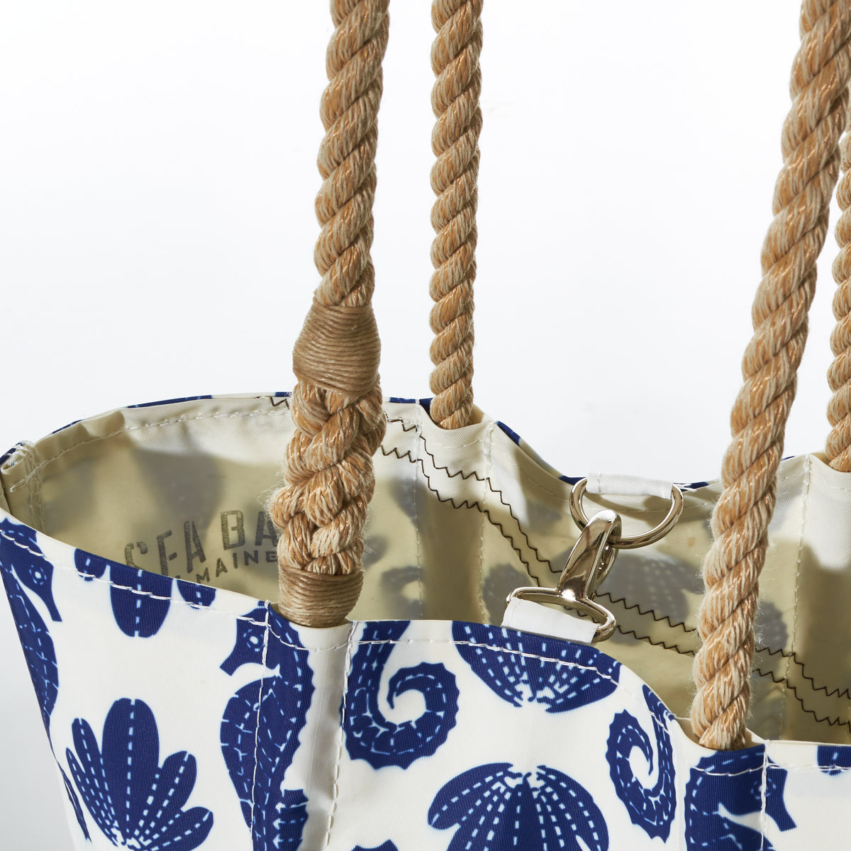 A close-up of the Blue Sea Horse Print Handbag by Sea Bags, featuring a white and blue seahorse design, tan rope handles, and a gold clasp inside.