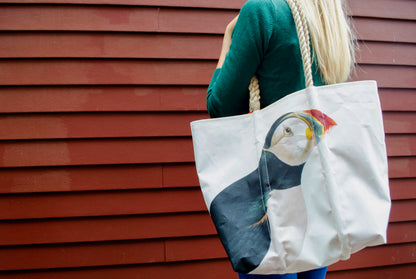 A person carrying a white Puffin Medium Tote by Sea Bags with rope handles featuring an Atlantic Puffin Audubon illustration.
