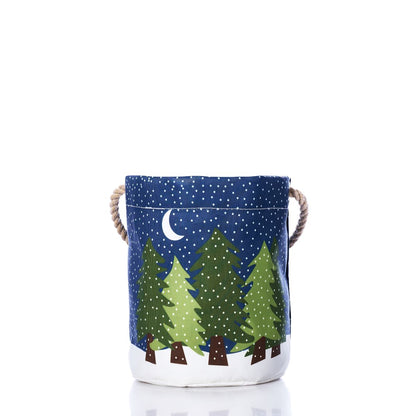 The Sea Bags Midnight Snow Bucket Bag is a reusable fabric storage basket with rope handles, featuring a pattern of green pine trees, snow, and a crescent moon on a dark blue background. Expertly crafted from recycled sail cloth, it combines eco-friendly materials with stylish design. by Sea Bags