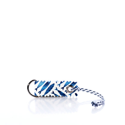 Introducing the Fish Print Sail Bag Charm by Sea Bags—a unique rectangular keychain crafted from upcycled sail cloth, featuring a distinctive blue and white fish pattern. Complete with a keyring and braided string, this eco-friendly accessory brings nautical flair and sustainable style to your collection. by Sea Bags