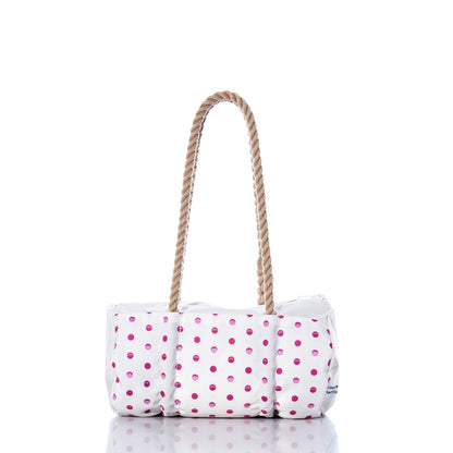 The Flip Side Summer Dots Baguette Bag by Sea Bags features a white tote design adorned with pink polka dots, a cushioned body, and two brown rope handles. Displayed on a reflective surface against a white background, this charming summer handbag blends playful style with everyday practicality. by Sea Bags