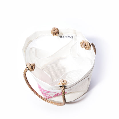 The Pink Lobster Beachcomber Bucket by Sea Bags is a white canvas beach bag crafted from recycled sail cloth, featuring sturdy rope handles with large knotted loops. The Sea Bags logo accents the inner rim, while a pink lobster design adds a distinctive touch to the exterior. This unique bucket bag blends style and sustainability—perfect for your seaside adventures. by Sea Bags
