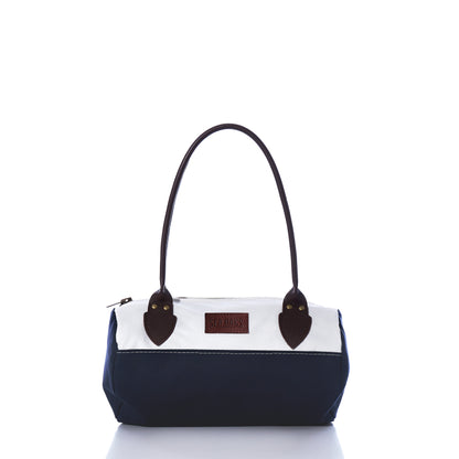 The Chebeague Baguette Bag by Sea Bags is a small, two-tone handbag crafted from recycled sailcloth, featuring a dark blue bottom, white top section, brown handles, and a visible rectangular Sea Bags label on the front. by Sea Bags