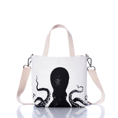 The Sea Bags Octopus Crossbody Tote, crafted from recycled sailcloth, features a black octopus illustration, beige handles, and an adjustable beige shoulder strap, and is displayed on a reflective surface. by Sea Bags