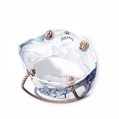 The Maine Fishing Village Essential Handbag by Sea Bags, crafted from recycled sail cloth and featuring white and blue canvas with rope handles and knotted corners, is inspired by the Maine coast. The SEA BAGS label is displayed on the inner lining, and the bag is photographed against a white background. by Sea Bags