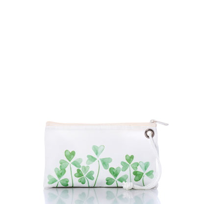 The Sea Bags Field of Clover Wristlet is crafted from recycled sailcloth for eco-friendly style, featuring green four-leaf clover designs, a white zipper, and a white cord loop. It is displayed on a reflective white surface. by Sea Bags