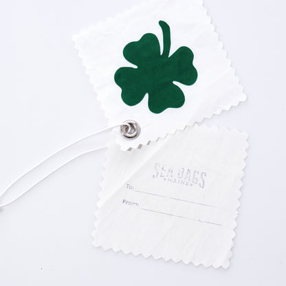 The Four Leaf Clover Sail Cloth Gift Tag by Sea Bags is crafted from white recycled sail cloth and features a green four-leaf clover design. Paired with a second tag labeled Sea Bags Maine and offering convenient To and From lines, both tags are joined by a sturdy white cord threaded through a metal grommet, making this accessory a sustainable way to personalize your gifts. by Sea Bags