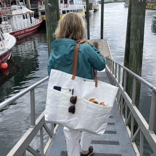 Woman with a large white tote bag walking on a dock with boats in the background