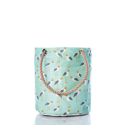 Introducing the Sea Bags Wharf Gulls Beachcomber Bucket—a light blue fabric tote with rope handles, adorned with a repeating pattern of stylized seagulls and yellow beaks on a white background. This charming beach bag features durable construction inspired by recycled sail cloth, making it perfect for seaside adventures while capturing a breezy coastal feel. by Sea Bags