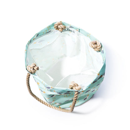 The Sea Bags Wharf Gulls Beachcomber Bucket is a cylindrical fabric bag crafted from recycled sail cloth, featuring a light blue patterned exterior, tan rope handles, and a white interior. Shown from above on a white background, it makes a stylish beach bag option. by Sea Bags