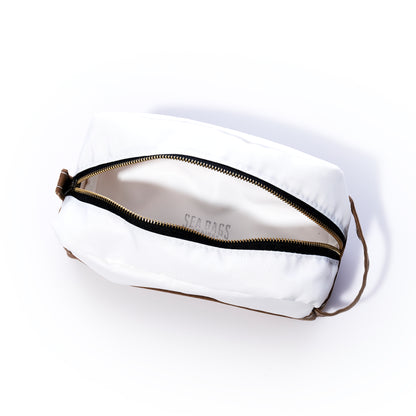 The Sea Bags Tan Chebeague Toiletry Bag is a rectangular white zippered pouch crafted from durable Dacron sailcloth, featuring a brown strap. Shown partially unzipped to display the interior, it is set against a white background. by Sea Bags