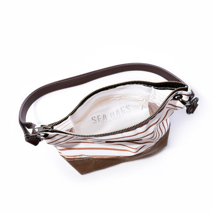 The Tan Chebeague Stripe Crossbody by Sea Bags is shown open, featuring brown and white stripes with a dark leather shoulder strap. Its white interior is labeled Sea Bags. Made from recycled sailcloth, the empty bag is displayed on a white background. by Sea Bags