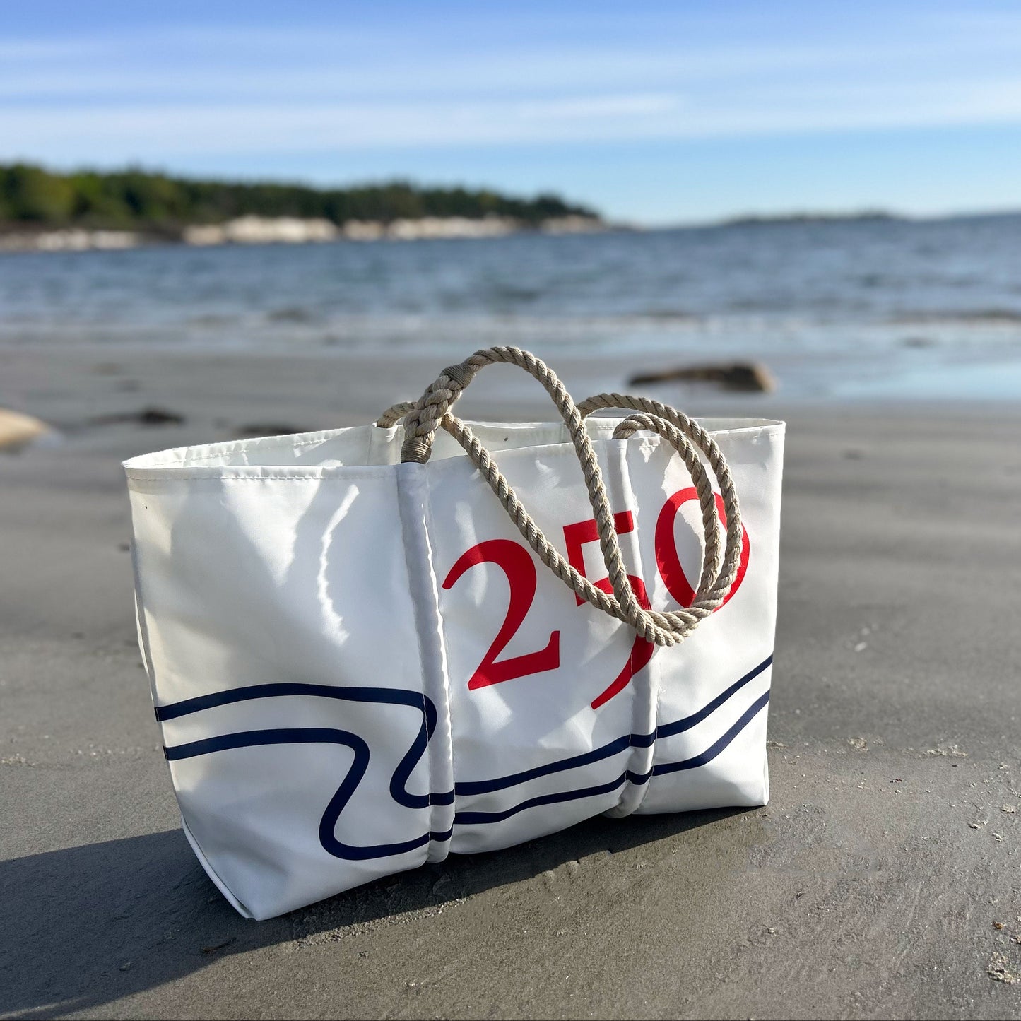 White bag with red text on a sandy beach with ocean in the background