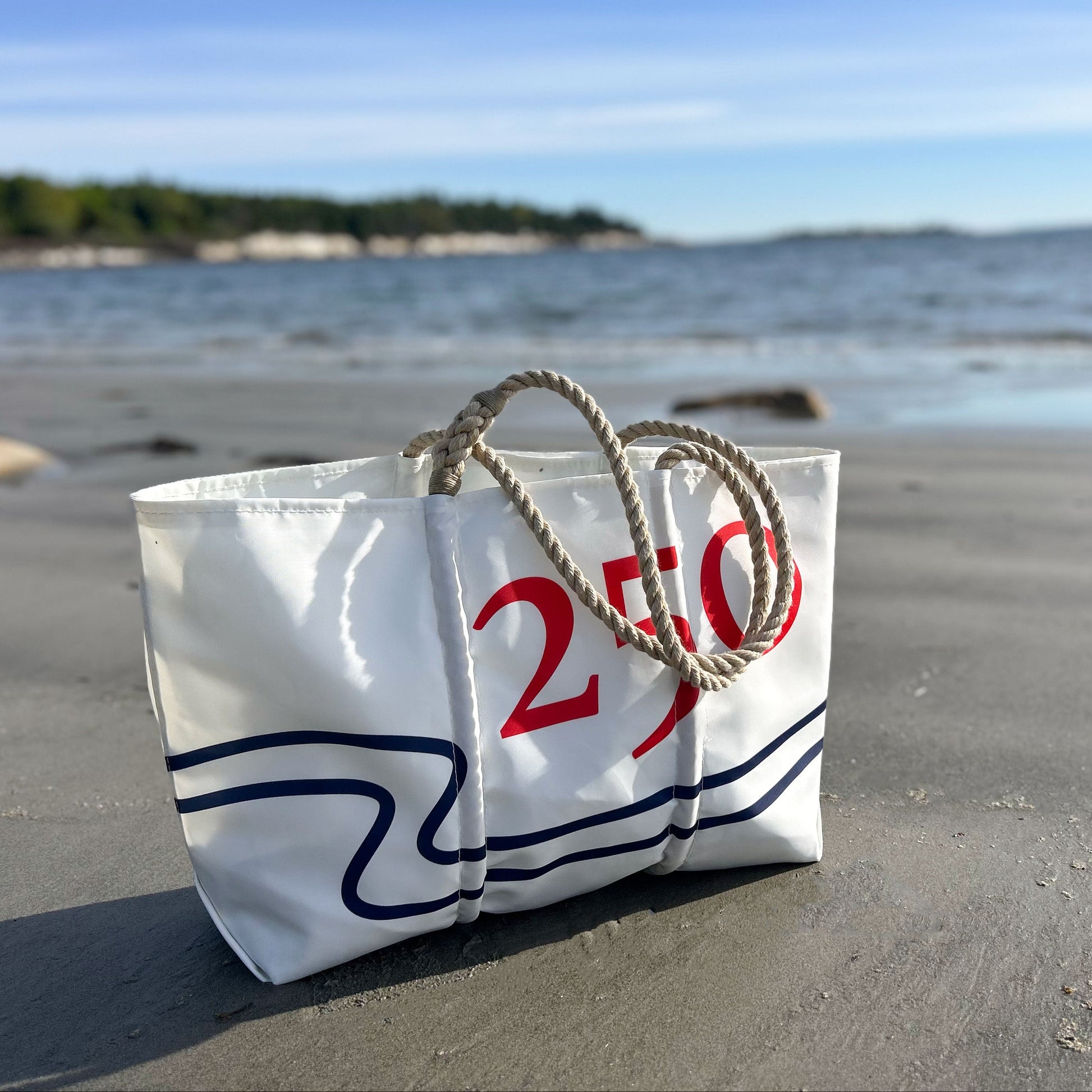 White bag with red text on a sandy beach with ocean in the background