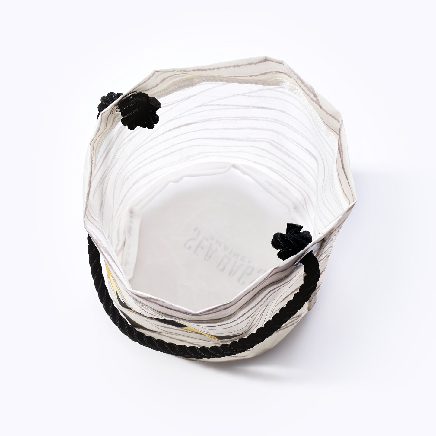 The Happy Mummy Bucket Bag by Sea Bags is a sustainable, white hexagonal fabric bucket crafted from recycled materials, featuring black rope handles and decorative black knots—shown from above on a white background, its the perfect eco-friendly addition to your bag collection. by Sea Bags