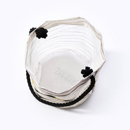 The Happy Mummy Bucket Bag by Sea Bags is a sustainable, white hexagonal fabric bucket crafted from recycled materials, featuring black rope handles and decorative black knots—shown from above on a white background, its the perfect eco-friendly addition to your bag collection. by Sea Bags