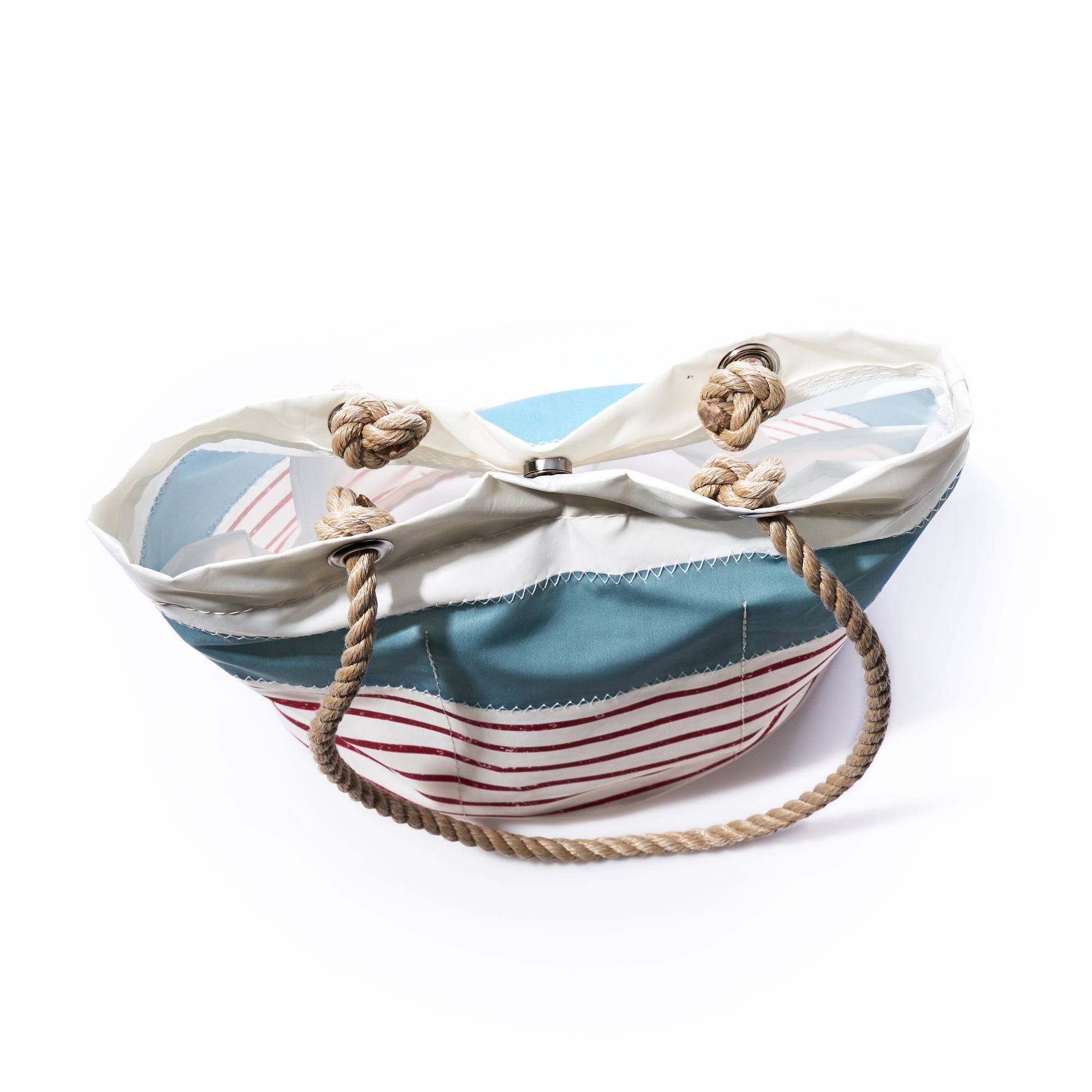 The Sea Bags Denim Blue-on-Red Mariner Stripe Essential Handbag, featuring bold red stripes, sturdy rope handles, and nautical knotted details, is displayed against a white background. This stylish and functional tote is perfect for everyday use.
