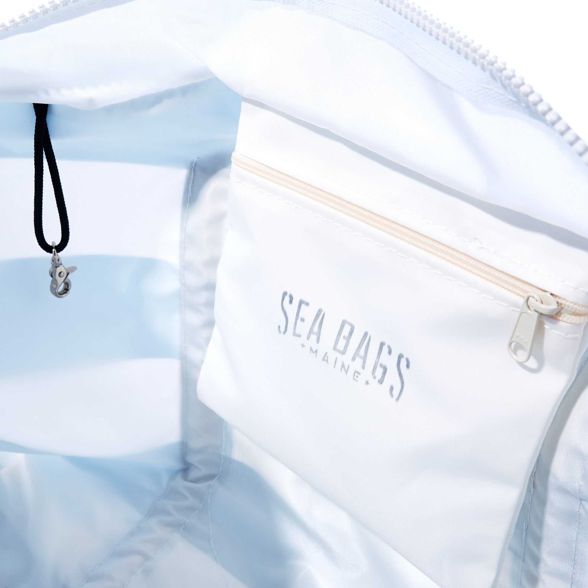 The Denim Blue Trolley Sleeve Travel Pier Tote by Sea Bags is crafted from recycled sailcloth material, shown open to reveal its spacious interior with a zippered pocket labeled Sea Bags Maine and a black cord with metal clasp. Thoughtfully designed, it features a convenient trolley sleeve for easy attachment to your luggage. by Sea Bags