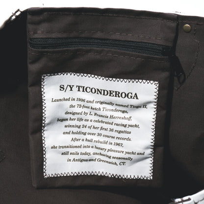 Interior pocket of a dark brown vintage sail cloth Heritage Ticonderoga Medium Tote, featuring a white rectangular patch that recounts the history of the yacht S/Y Ticonderoga.