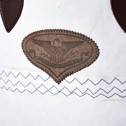 Heritage Ticonderoga Medium Tote in white vintage sail cloth, featuring a brown shield-shaped patch with an eagle emblem and two rows of blue zigzag stitching.