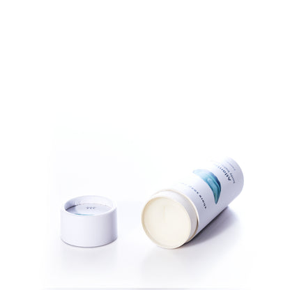 A white cylindrical container of Shore Soap Co’s Atlantic Eco-Friendly Body Balm Stick, featuring a blue label, lies on its side with the lid removed to reveal the concentrated moisturizer inside—formulated to deliver deep hydration for dry skin—set against a clean, white background.