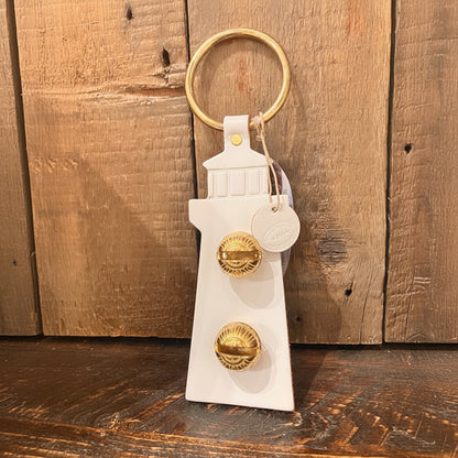 The White Lighthouse Door Chime by New England Bells features two brass knobs and a gold ring, its design inspired by classic New England Bells, showcased against a wooden background.
