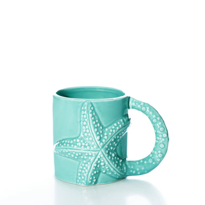 The Starfish Mug by Batela USA Inc features a turquoise ceramic design with a raised sea-star texture and a handle sculpted to follow the shape of the starfish. This ocean-themed mug is displayed on a white surface against a plain white background.