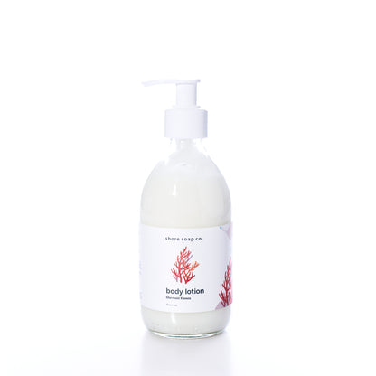 A clear bottle of Shore Soap Co Mermaid Kisses Eco-Friendly Body Lotion with a pump and white label featuring a red coral design.