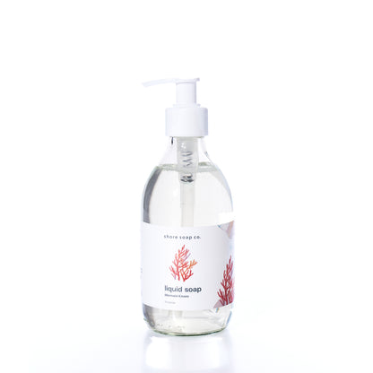 Clear glass pump bottle of Shore Soap Co. Mermaid Kisses Eco-Friendly Liquid Soap with a white label featuring a red coral design, displayed against a white background. Made with natural ingredients, this gentle formula is perfect for sensitive skin.