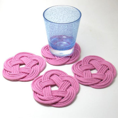 A blue glass rests on one of four pink Nautical Sailor Knot Coasters by Mystic Knotwork, each handmade in the USA from braided cotton rope, displayed on a white background.
