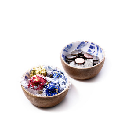 Two small bowls: the first, Batela USA Incs Enameled Wood Bowl - Striped Fish, features an enameled mango wood finish with a delicate striped fish design and holds assorted wrapped chocolates; the second contains various coins. Both bowls are displayed on a white background. by Sea Bags