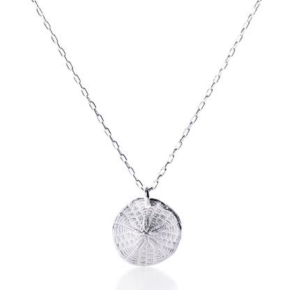 Pendant Necklace - Sand Dollar Silver by Maine Yoga Jewelry features a silver chain necklace with a textured, round sand dollar-inspired pendant, crafted sustainably and evoking the coastal beauty of Maine, shown against a white background. by Sea Bags