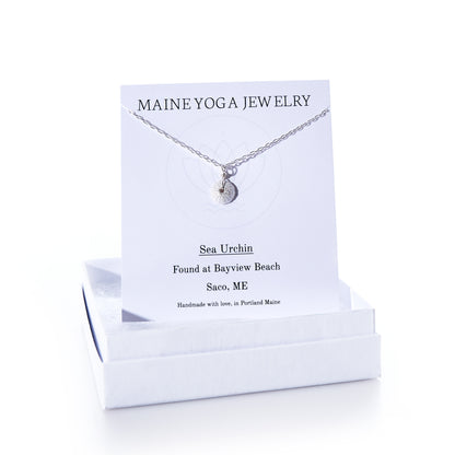 The Pendant Necklace - Tiny Sea Urchin Silver by Maine Yoga Jewelry features a handcrafted silver sea urchin pendant on a delicate silver chain, beautifully displayed on a branded Maine Yoga Jewelry card and presented in an elegant white jewelry box. by Sea Bags