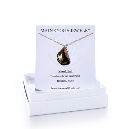 Pendant Necklace - Large Mussel Bronze displayed on a card labeled Maine Yoga Jewelry with descriptive text, set atop a white jewelry box. This elegant piece of coastal jewelry features a beautifully crafted large bronze mussel pendant—perfect for those who treasure seaside memories. by Sea Bags