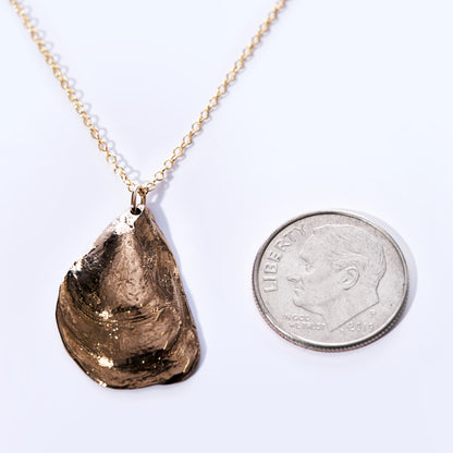 A Large Mussel Bronze Pendant Necklace by Maine Yoga Jewelry, ideal for coastal jewelry lovers, is displayed next to a dime for scale on a white background. by Sea Bags