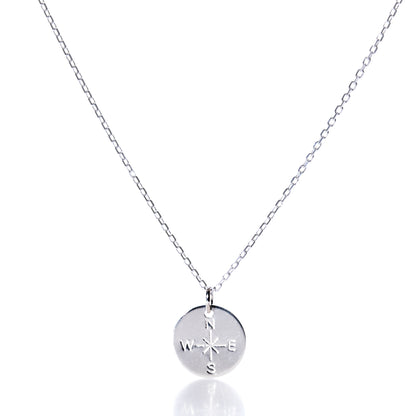 Discover the Pendant Necklace - Silver Compass Rose by Maine Yoga Jewelry, featuring a round silver pendant engraved with a compass rose showing N, S, E, and W directions. This nautical necklace is displayed on a simple chain against a white background and is proudly made in Maine. by Sea Bags