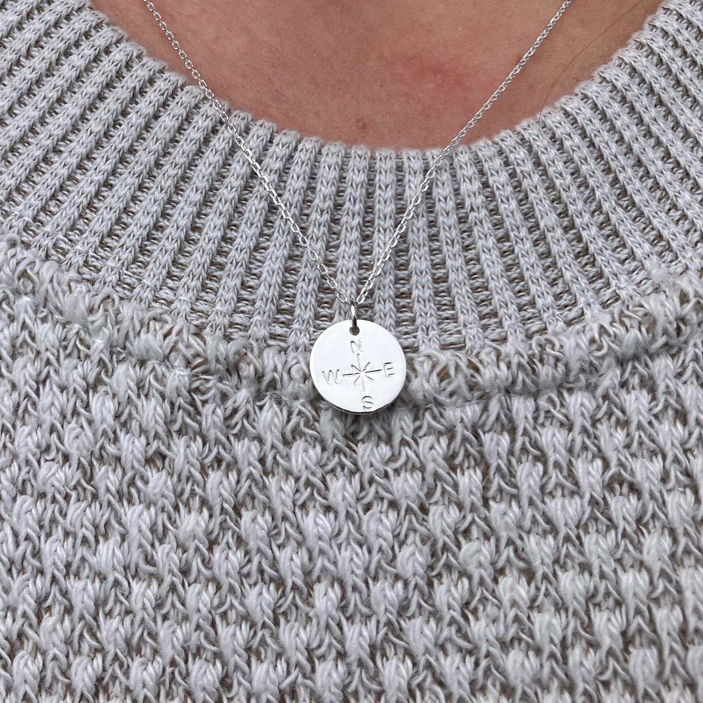 Silver necklace with a round pendant on a gray knitted sweater