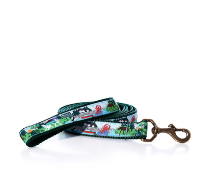 Coiled green Vacationland Dog Leash by Belted Cow, featuring a repeating pattern of lobsters, lighthouses, and moose, finished with a bronze-toned metal clip.